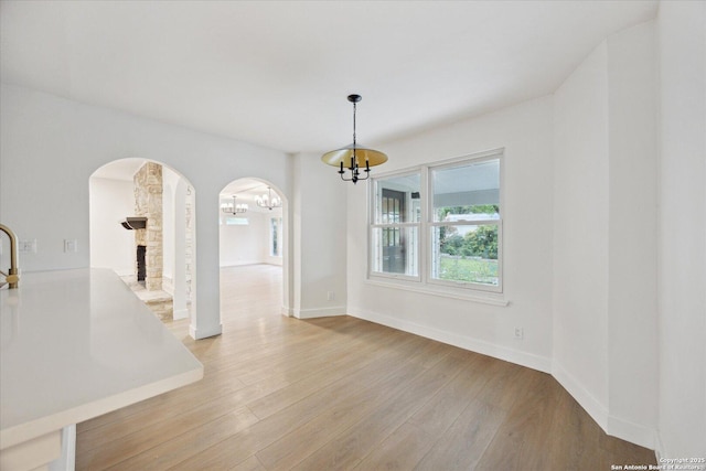 unfurnished dining area with arched walkways, an inviting chandelier, baseboards, and light wood-type flooring