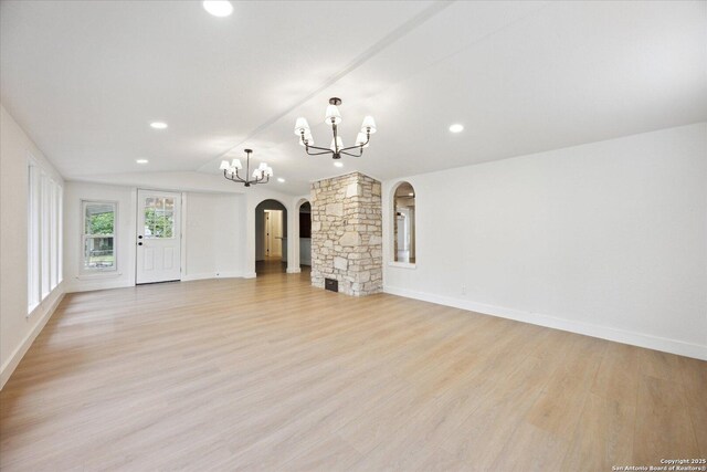 unfurnished living room with light wood finished floors, an inviting chandelier, baseboards, arched walkways, and lofted ceiling