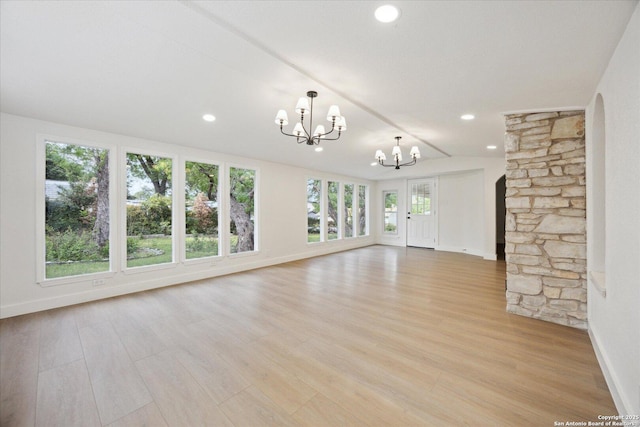 unfurnished living room featuring arched walkways, light wood-style flooring, a chandelier, and baseboards