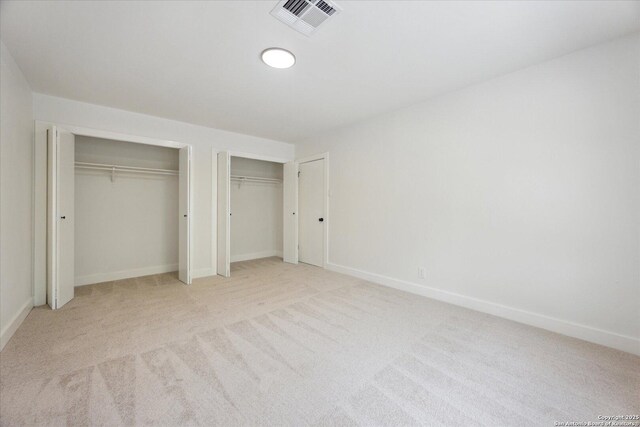 unfurnished bedroom featuring baseboards, visible vents, two closets, and carpet flooring