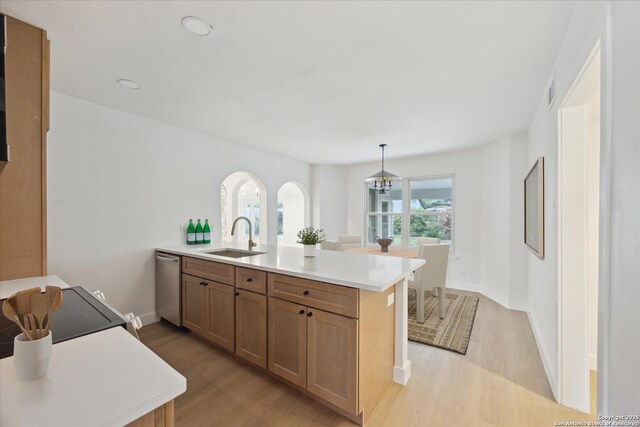 kitchen featuring stainless steel dishwasher, light wood-style flooring, light countertops, a sink, and a peninsula
