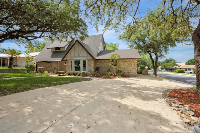 tudor-style house featuring concrete driveway, a front yard, a shingled roof, and stone siding