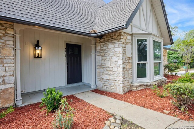property entrance with a shingled roof and stone siding