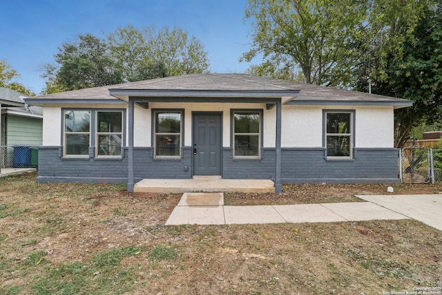 view of front of house featuring a shingled roof, stucco siding, covered porch, fence, and brick siding