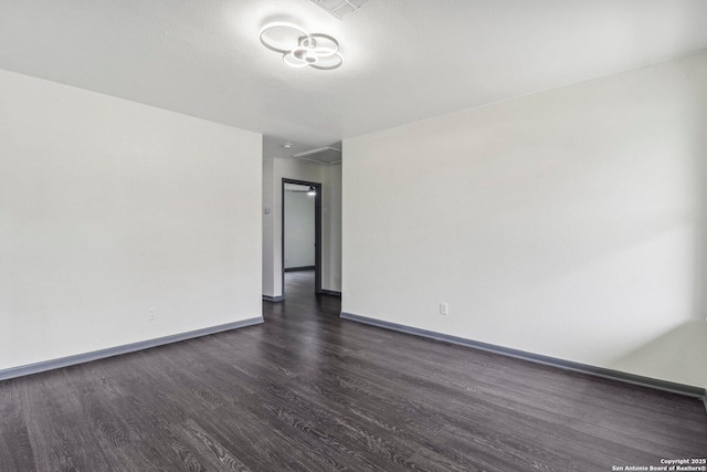 unfurnished room with attic access, dark wood-style floors, and baseboards