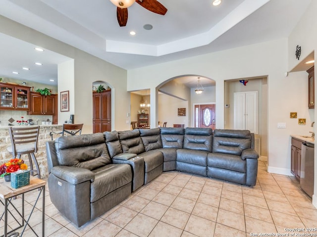 living area with light tile patterned floors, ceiling fan, a tray ceiling, arched walkways, and recessed lighting