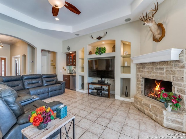 living area featuring light tile patterned floors, built in features, a tray ceiling, a ceiling fan, and arched walkways
