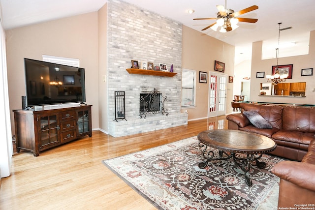 living room with a brick fireplace, wood finished floors, high vaulted ceiling, and ceiling fan with notable chandelier