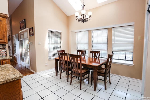 dining space with light tile patterned floors, baseboards, an inviting chandelier, high vaulted ceiling, and a skylight