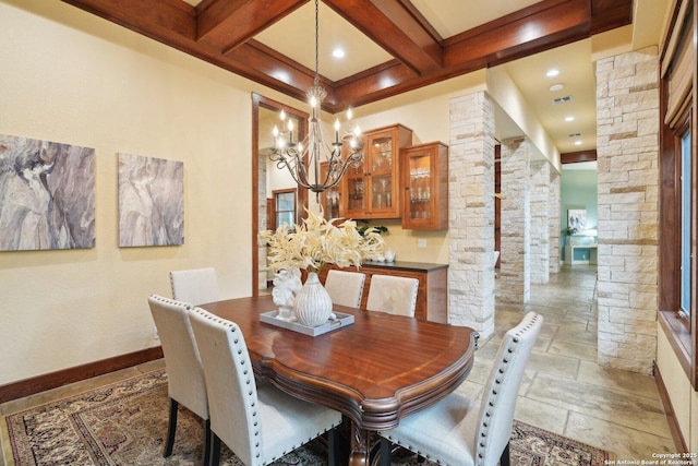 dining area with beamed ceiling, stone tile flooring, coffered ceiling, an inviting chandelier, and decorative columns