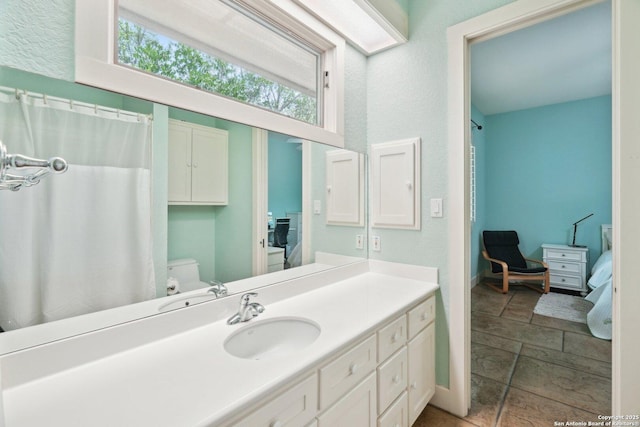 bathroom with vanity, curtained shower, stone finish flooring, toilet, and baseboards