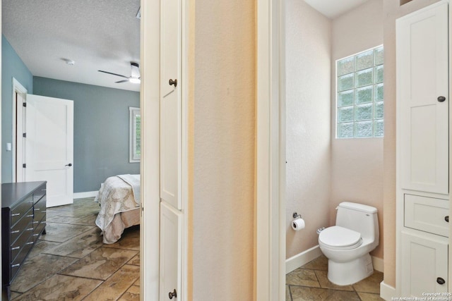 bathroom with stone tile floors, ceiling fan, toilet, baseboards, and ensuite bathroom