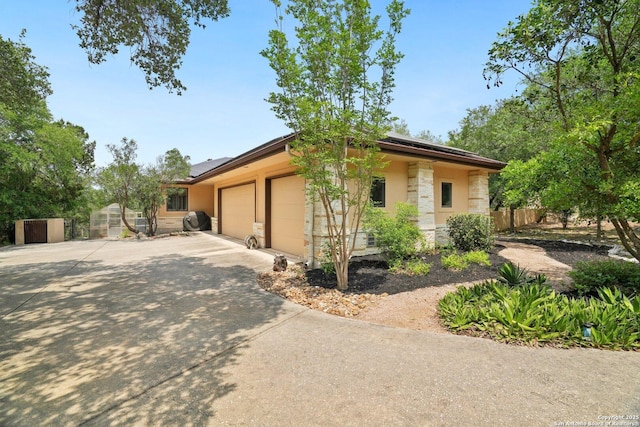 view of side of home with a garage, driveway, stone siding, solar panels, and fence
