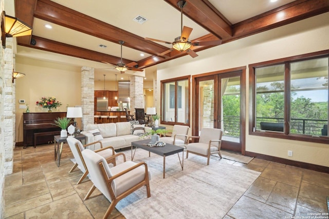 living room featuring beamed ceiling, stone tile flooring, a ceiling fan, visible vents, and baseboards