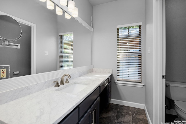 bathroom with toilet, plenty of natural light, vanity, and baseboards