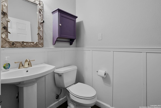 bathroom featuring toilet, a wainscoted wall, and a decorative wall