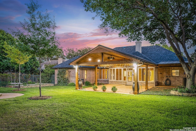 back of property featuring fence, a patio, a chimney, a lawn, and brick siding