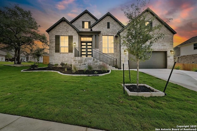 view of front of house featuring driveway, a yard, stone siding, and a garage