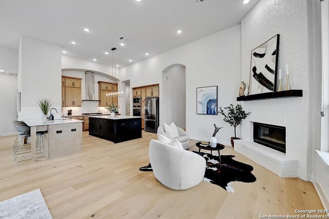 living area with light wood finished floors, recessed lighting, a brick fireplace, baseboards, and arched walkways