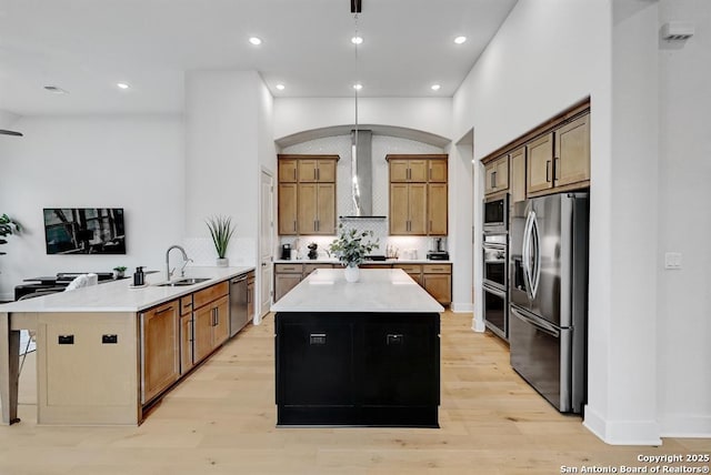 kitchen featuring a sink, stainless steel appliances, a center island, a peninsula, and wall chimney range hood