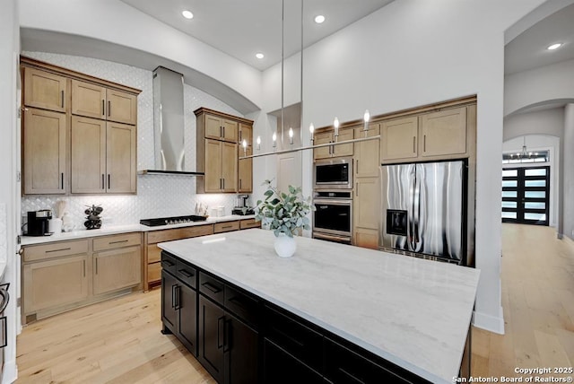 kitchen featuring light wood-style floors, arched walkways, wall chimney exhaust hood, and appliances with stainless steel finishes