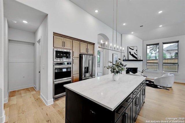 kitchen featuring open floor plan, stainless steel appliances, light wood-style flooring, and a center island