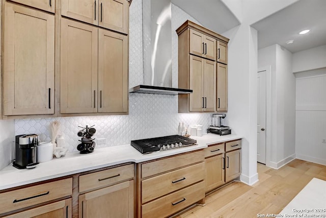 kitchen with light wood finished floors, stainless steel gas cooktop, wall chimney exhaust hood, backsplash, and light countertops