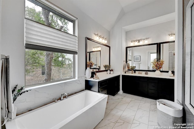 full bathroom with lofted ceiling, vanity, a freestanding tub, and marble finish floor