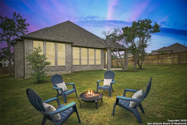 rear view of property with a lawn, a fire pit, a shingled roof, and a fenced backyard