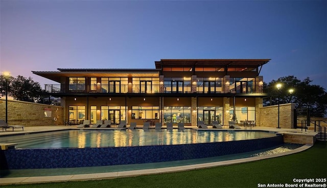 rear view of property with a patio, an infinity pool, and a balcony