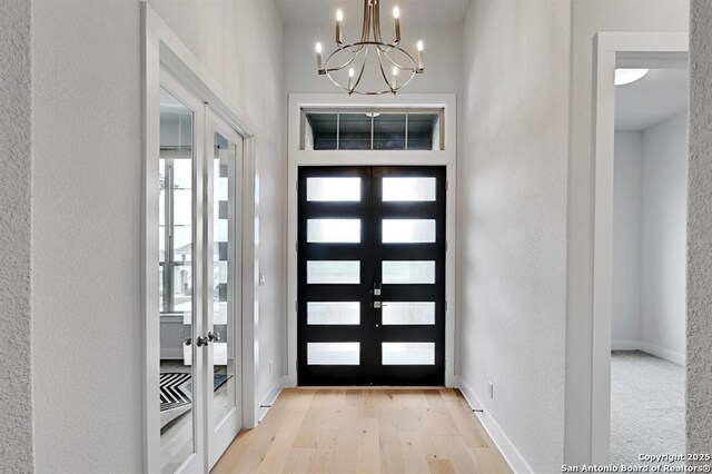 entrance foyer with baseboards, an inviting chandelier, french doors, and light wood-style flooring