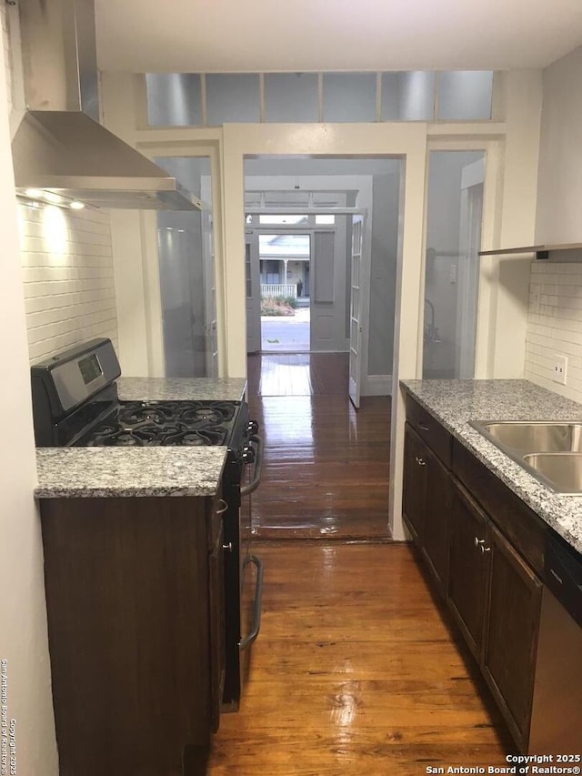 kitchen with decorative backsplash, appliances with stainless steel finishes, dark brown cabinets, dark wood-style floors, and wall chimney exhaust hood