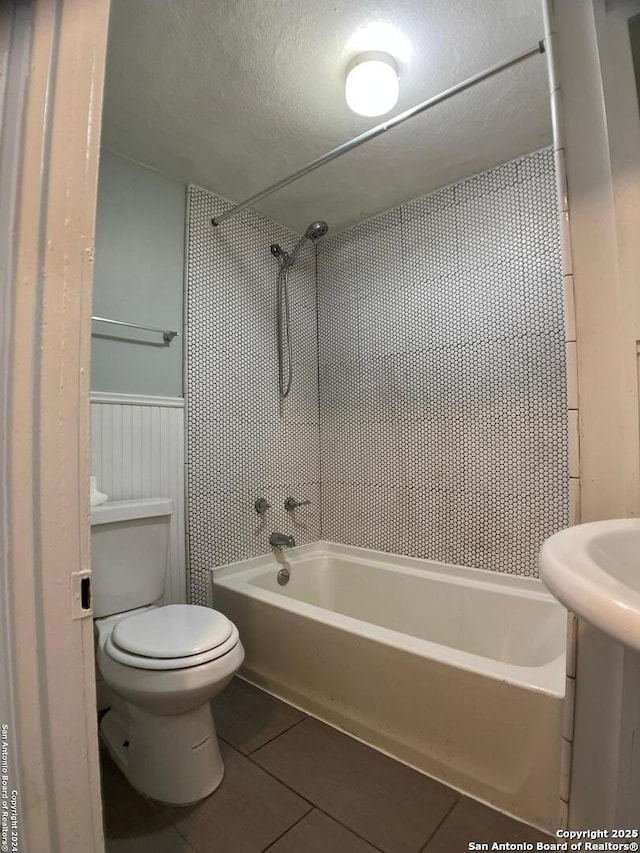 bathroom with a textured ceiling, shower / washtub combination, toilet, and tile patterned flooring