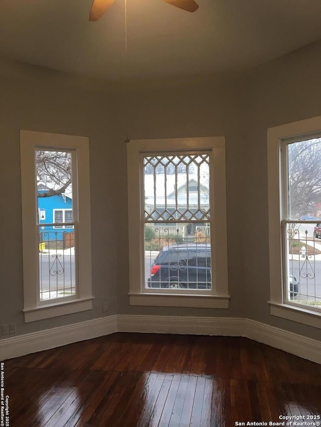 unfurnished room with ceiling fan, baseboards, a wealth of natural light, and dark wood-type flooring