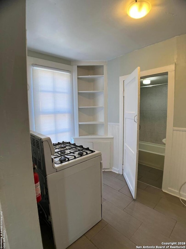 kitchen featuring light tile patterned floors, a wainscoted wall, and white gas range oven