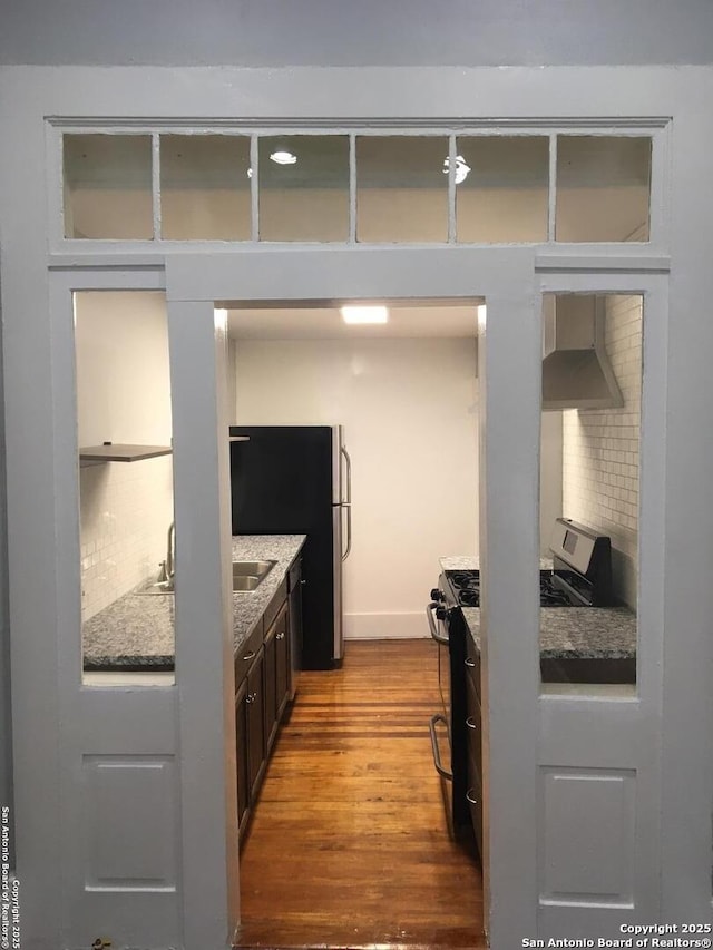 kitchen with tasteful backsplash, wood finished floors, appliances with stainless steel finishes, and wall chimney range hood