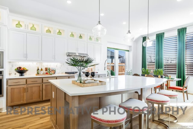 kitchen featuring a kitchen breakfast bar, pendant lighting, decorative backsplash, light countertops, and light wood-type flooring