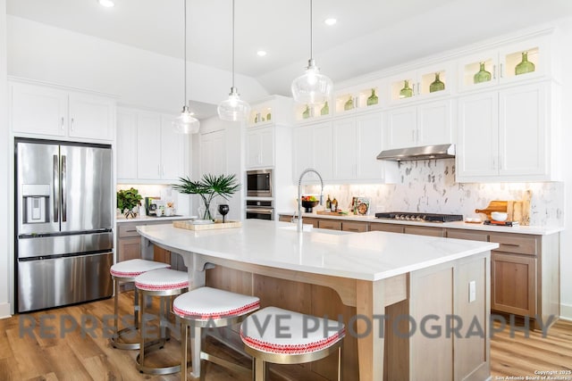 kitchen featuring wood finished floors, stainless steel appliances, an island with sink, and under cabinet range hood