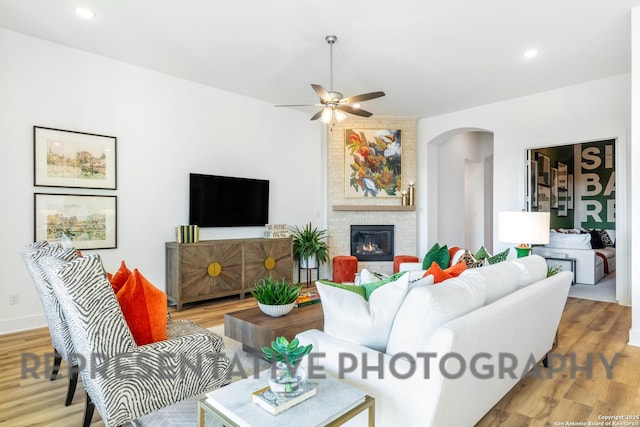 living room featuring recessed lighting, arched walkways, wood finished floors, a fireplace, and a ceiling fan