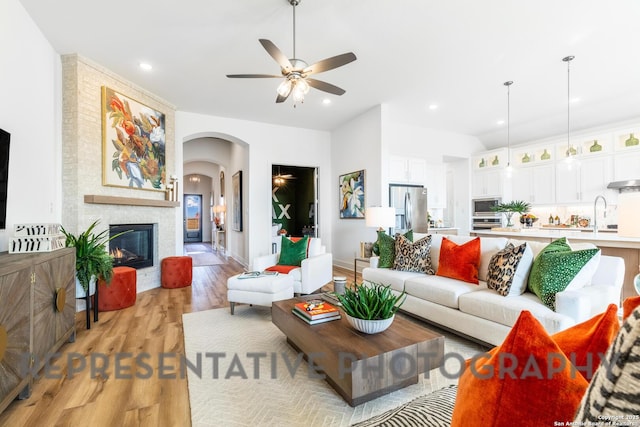 living area with arched walkways, light wood-style flooring, a large fireplace, ceiling fan, and baseboards