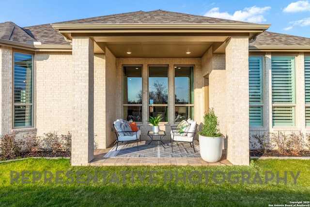 entrance to property featuring roof with shingles, a patio, and brick siding