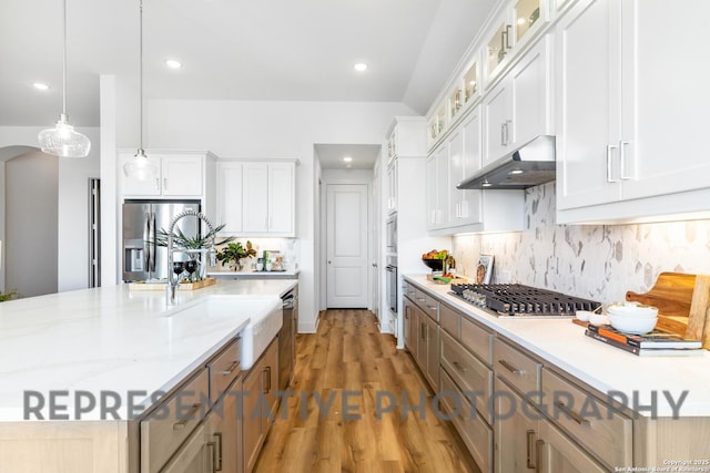 kitchen with wood finished floors, decorative backsplash, under cabinet range hood, appliances with stainless steel finishes, and white cabinetry
