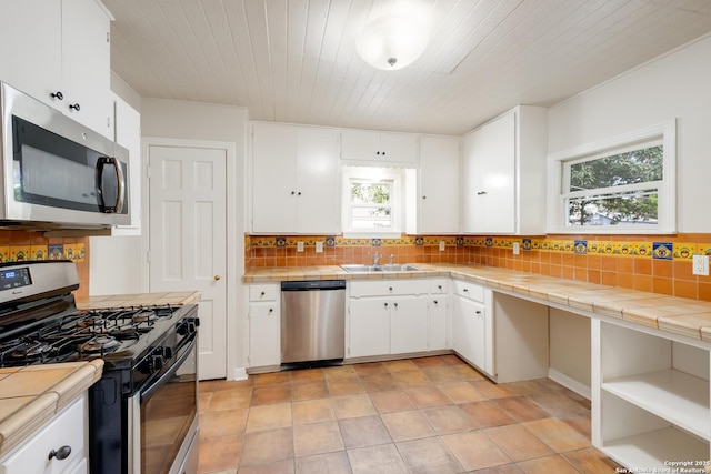 kitchen with tile countertops, a sink, appliances with stainless steel finishes, and a wealth of natural light