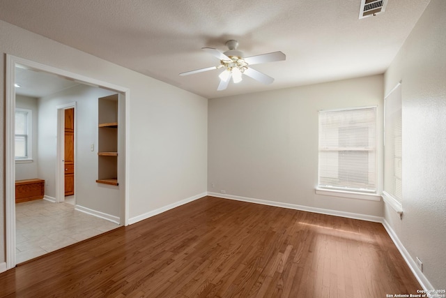 spare room with baseboards, visible vents, wood finished floors, and a ceiling fan