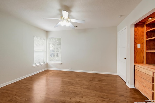 empty room featuring a ceiling fan, visible vents, baseboards, and dark wood-type flooring