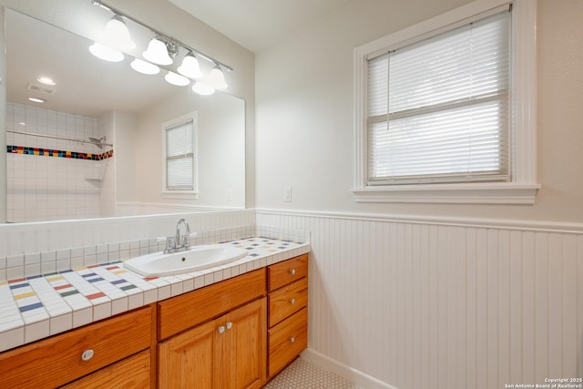 bathroom with plenty of natural light, vanity, a wainscoted wall, and tiled shower