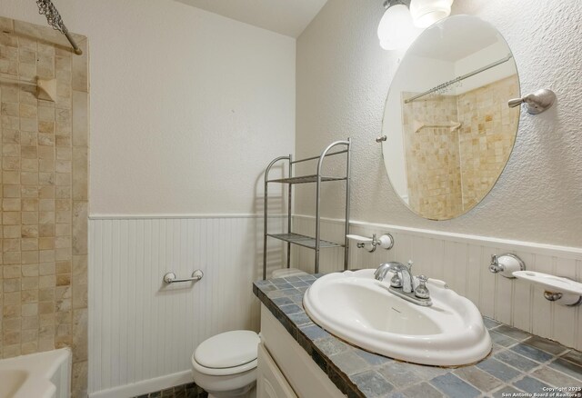 bathroom featuring toilet, a wainscoted wall, shower / bath combination, and vanity