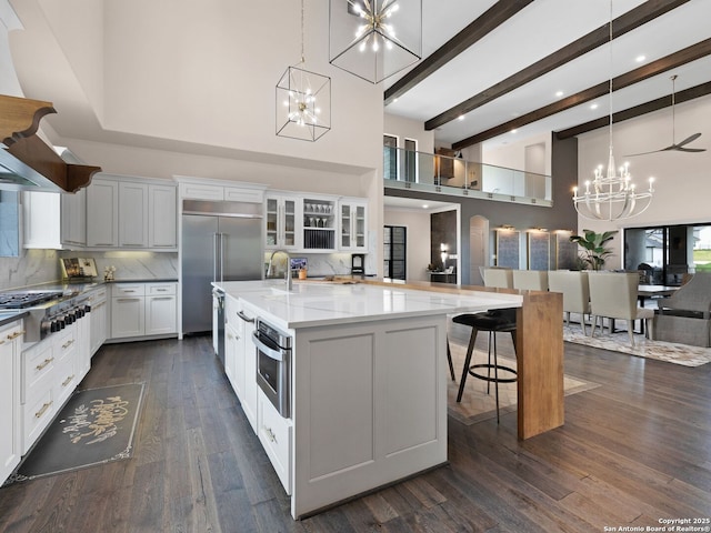 kitchen with glass insert cabinets, appliances with stainless steel finishes, an inviting chandelier, a large island with sink, and a high ceiling