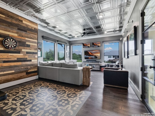 living area featuring baseboards, wood walls, ornamental molding, an ornate ceiling, and dark wood-style floors
