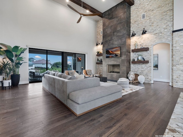 living room featuring beam ceiling, arched walkways, ceiling fan, and a high ceiling